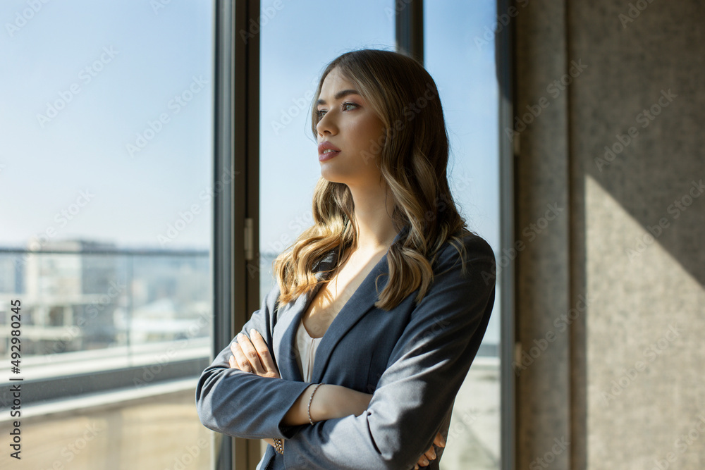 Businesswoman wearing suit thinking and looking outdoors through a window at office