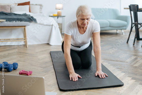 elderly woman doing fitness with an online trainer in her living room.