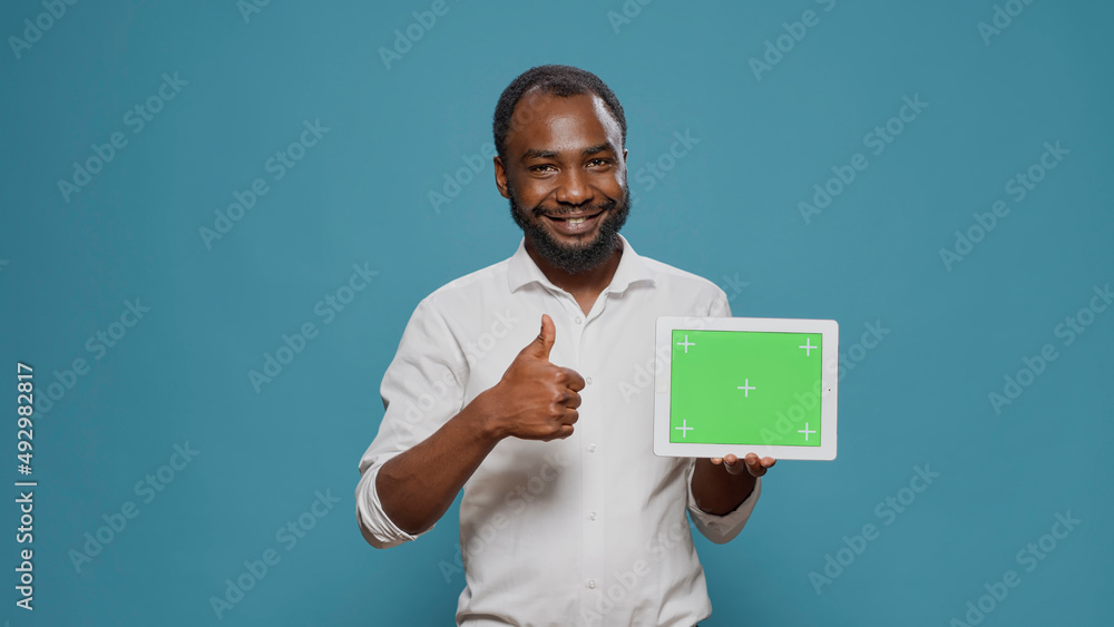 Happy man pointing at digital tablet with horizontal green screen in hand, showng isolated copy space with blank chroma key template and mockup background. Modern display technology.