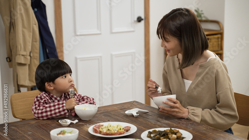 loving Asian mother showing concern to her baby son during dinner time at home. she asks the boy if he wants some meat and put one piece in his bowl