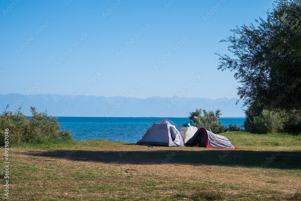Tourists tents on Issyk-kol lake wild beach. Travel, tourism, recreation in Kyrgyzstan concept. Summer vacation.