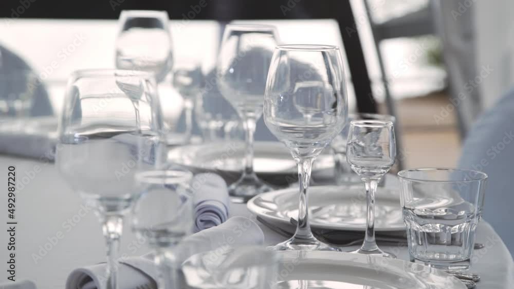 Clean and empty sets of three glasses stand near plates and textile napkins on banquet table. Stylish light serving of round table, arrangement of dishes. Clean and empty sets of three glasses stand near plates and textile napkins on banquet table. Stylish light serving of round table, arrangement of dishes.