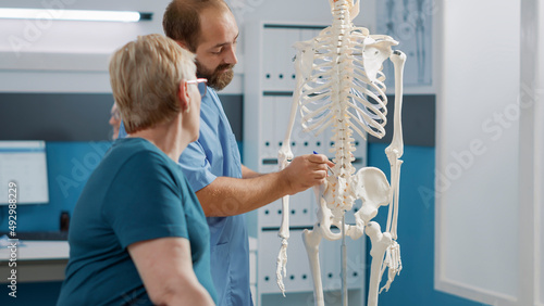 Foto Male doctor pointing at human skeleton to show spinal cord and explain mechanical disorders in rehabilitation cabinet
