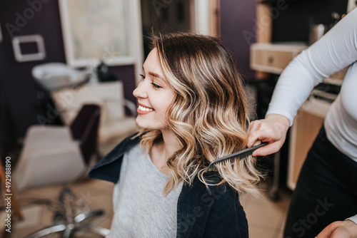 Beautiful young woman with perfect hairstyle satisfied after dyeing hair and making highlights in hair salon.
