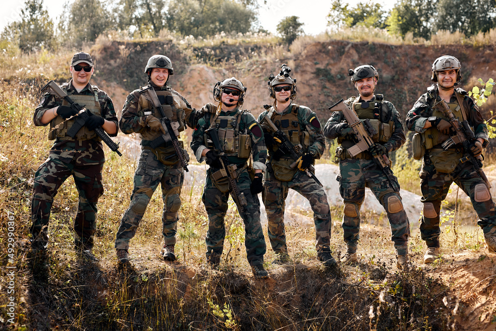 group of equipped and armed special forces soldiers standing in field. Concept of military anti-terrorism operations, special operations of NATO forces. Team posing at camera together group of equipped and armed special forces soldiers standing in field. Concept of military anti-terrorism operations, special operations of NATO forces. Team posing at camera together