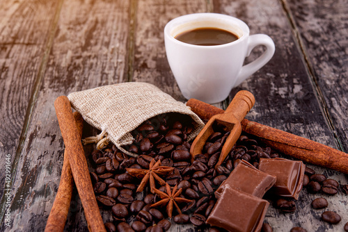 cup of coffee with chocolate, cinnamon sticks, and coffee beans on wooden background