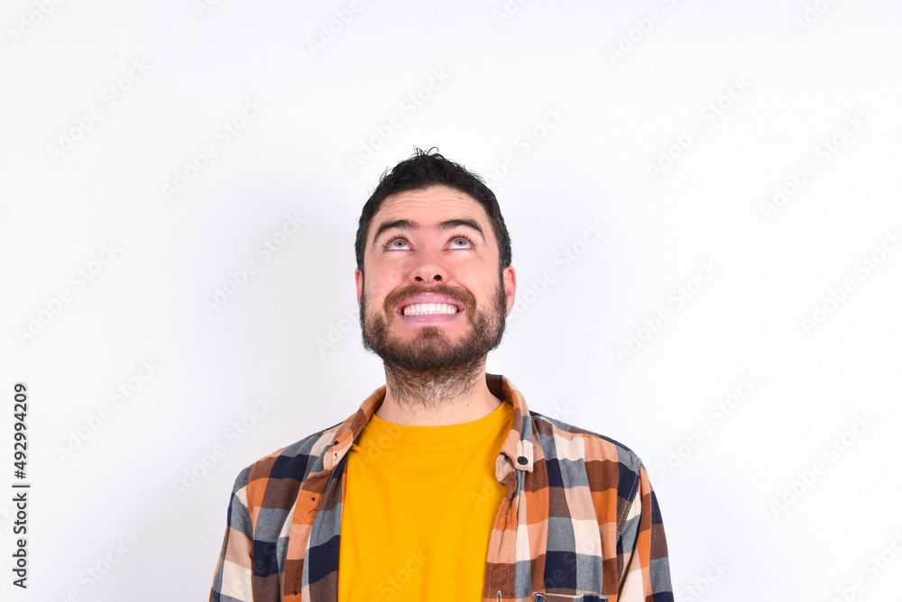 Portrait of mysterious young caucasian man wearing plaid shirt over white background looking up with enigmatic smile. Advertisement concept. Portrait of mysterious young caucasian man wearing plaid shirt over white background looking up with enigmatic smile. Advertisement concept.