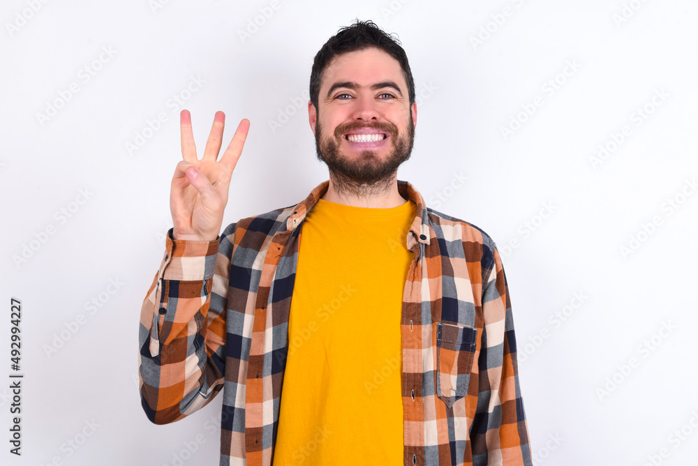 Naklejka premium young caucasian man wearing plaid shirt over white background showing and pointing up with fingers number three while smiling confident and happy.