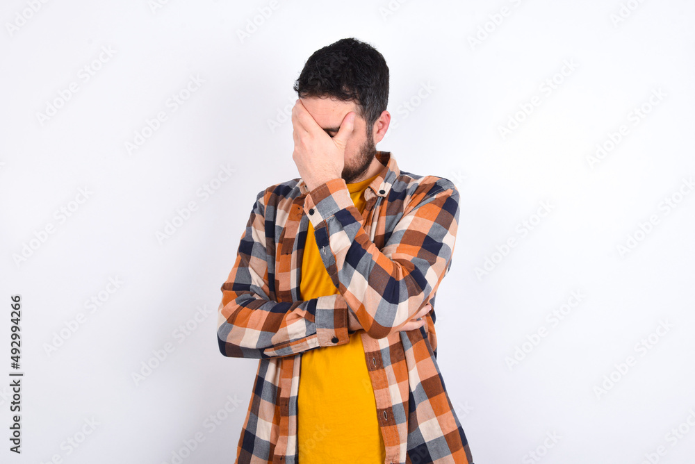 young caucasian man wearing plaid shirt over white background making facepalm gesture while smiling amazed with stupid situation. young caucasian man wearing plaid shirt over white background making facepalm gesture while smiling amazed with stupid situation.