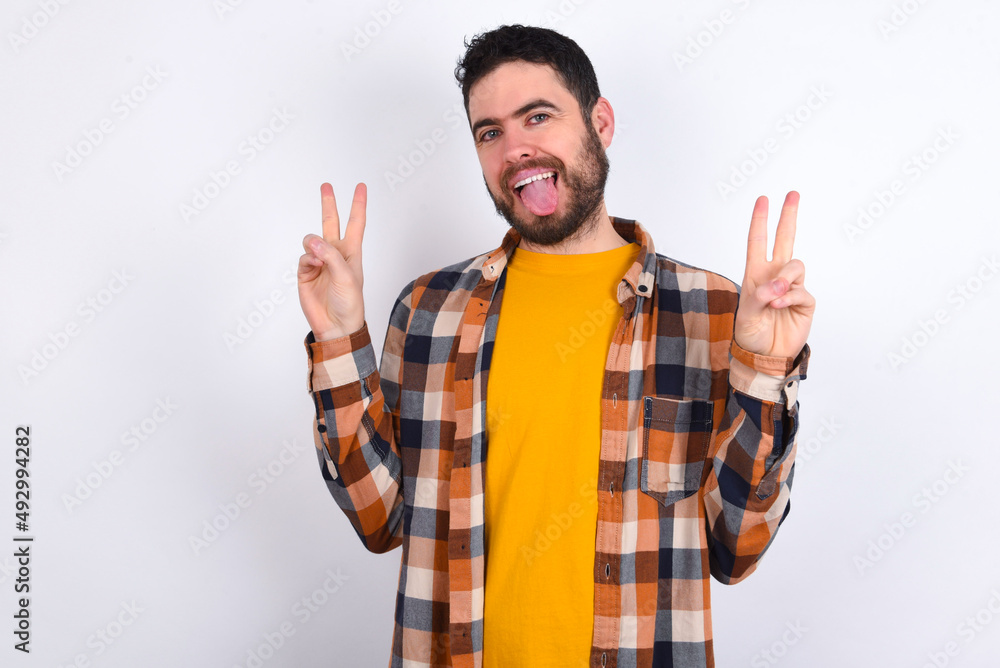young caucasian man wearing plaid shirt over white background with optimistic smile, showing peace or victory gesture with both hands, looking friendly. V sign. young caucasian man wearing plaid shirt over white background with optimistic smile, showing peace or victory gesture with both hands, looking friendly. V sign.