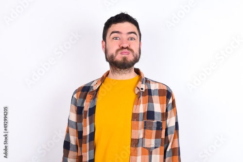 young caucasian man wearing plaid shirt over white background puffing cheeks with funny face. Mouth inflated with air, crazy expression.