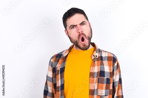 Expressive facial expressions. Shocked stupefied young caucasian man wearing plaid shirt over white background, keeps jaw dropped feels stunned from what he sees aside.