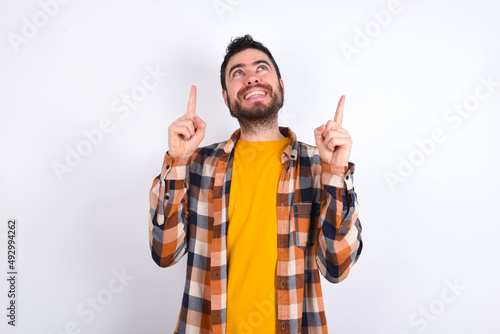 Bild auf Leinwand Successful friendly looking young caucasian man wearing plaid shirt over white background exclaiming excitedly, pointing both index fingers up, indicating something