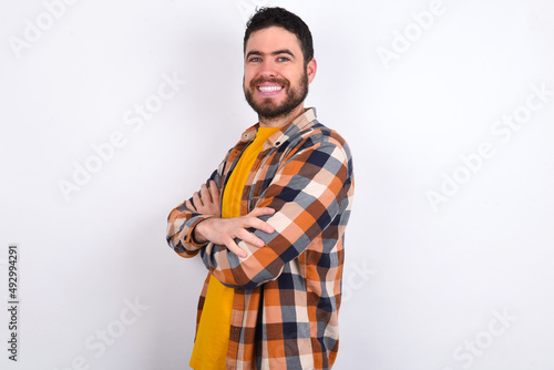 Image of cheerful young caucasian man wearing plaid shirt over white background with arms crossed. Looking and smiling at the camera. Confidence concept.