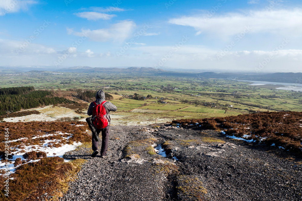 Male tourist with red backpack on a footpath in a mountains. County Sligo, Ireland. Cold winter season. Outdoor sport and activity. Travel and sport concept. Beautiful Irish nature in the background Male tourist with red backpack on a footpath in a mountains. County Sligo, Ireland. Cold winter season. Outdoor sport and activity. Travel and sport concept. Beautiful Irish nature in the background