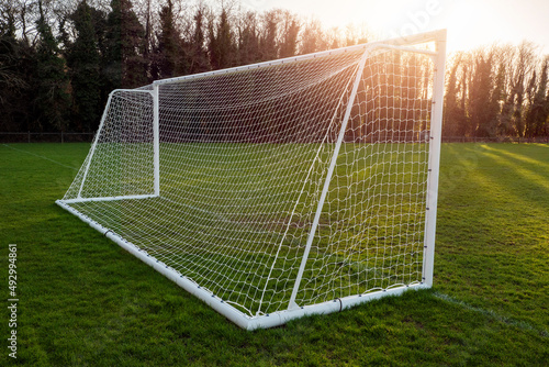 Football or soccer goal post on a training ground in a park at sunset. Warm color. Sun flare. Nobody. Outdoor activity. Calm nature background