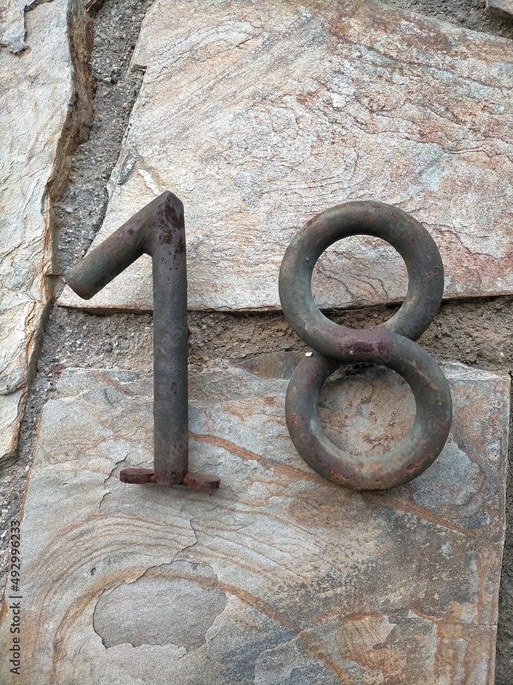Number eighteen, 18 in number. Made of metal with a rustic stone background with a cement seam. Number eighteen, 18 in number. Made of metal with a rustic stone background with a cement seam.