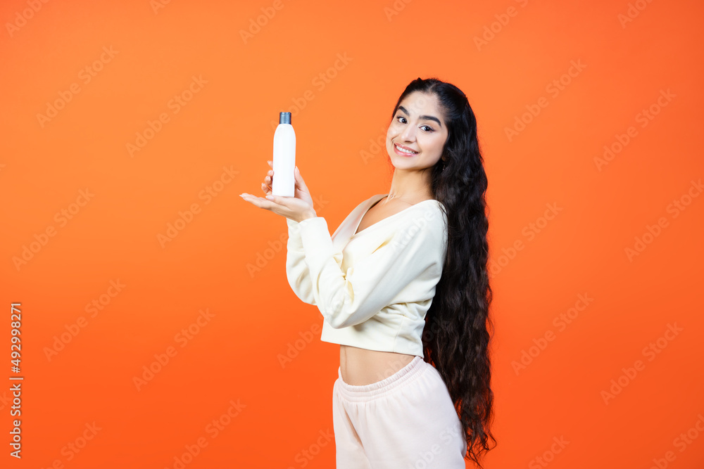 Beautiful mixed race woman with empty mockup shampoo bottle on orange background. Beautiful mixed race woman with empty mockup shampoo bottle on orange background.