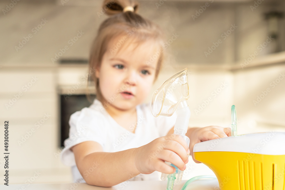Little caucasian girl is breathing with special mask, which helps to stop asthma attack or relieve symptoms of respiratory disease. Child making inhalation with nebulizer at home Little caucasian girl is breathing with special mask, which helps to stop asthma attack or relieve symptoms of respiratory disease. Child making inhalation with nebulizer at home