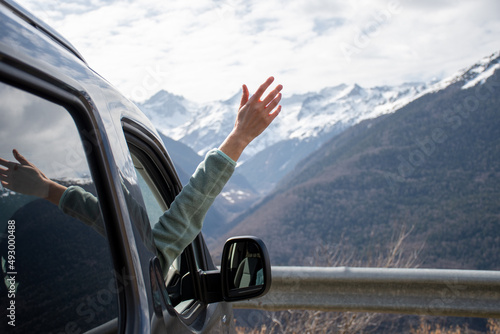 Young woman sticking her hand out the window of her van and enjoying the view towards the snowy mountains of the pyrenees
