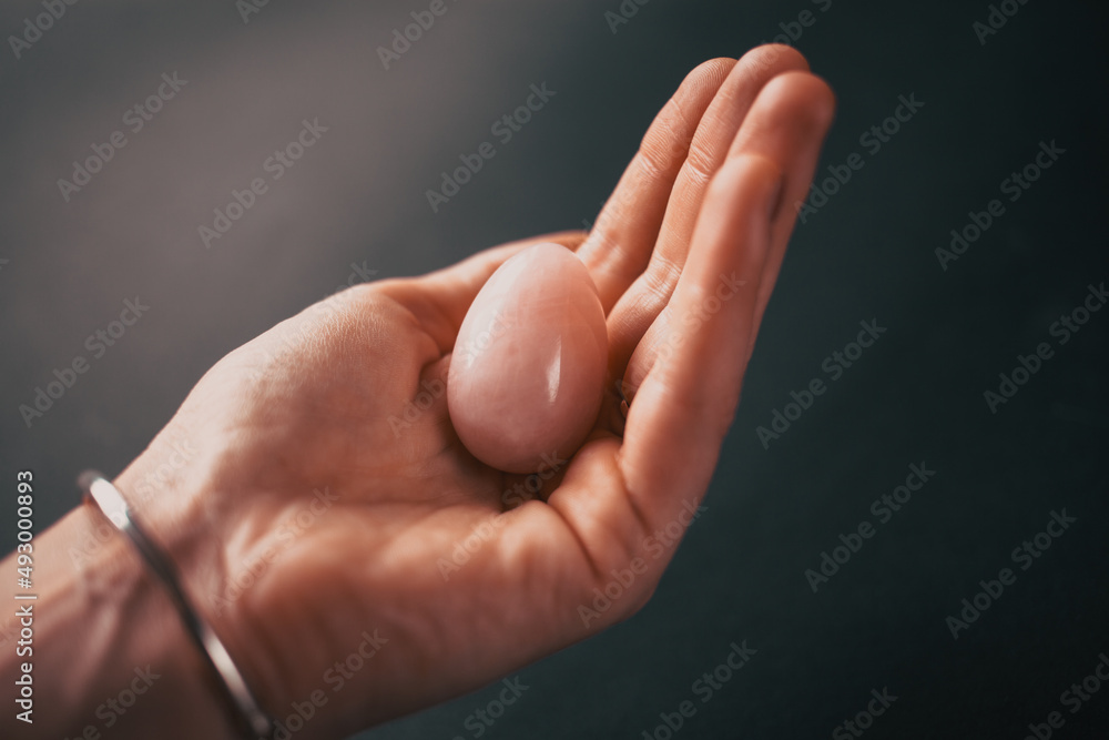 woman holding in hand a vaginal (yoni) egg. Rose quartz crystal jade egg. Copy space