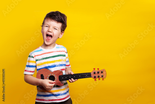 funny boy playing guitar. A child with a guitar on a yellow background in the studio. Emotions. The child emotionally plays the guitar and sings