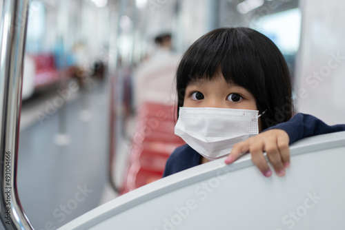 Little girl with surgical mask face protection flu and Virus outbreak in public transportation (skytrain or subway). Concept of New normal lifestyle, Using public transport to travel to school.