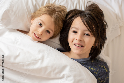 Brothers, blond toddler boy and older preteen boy, cuddling in bed in the morning, love and tenderness