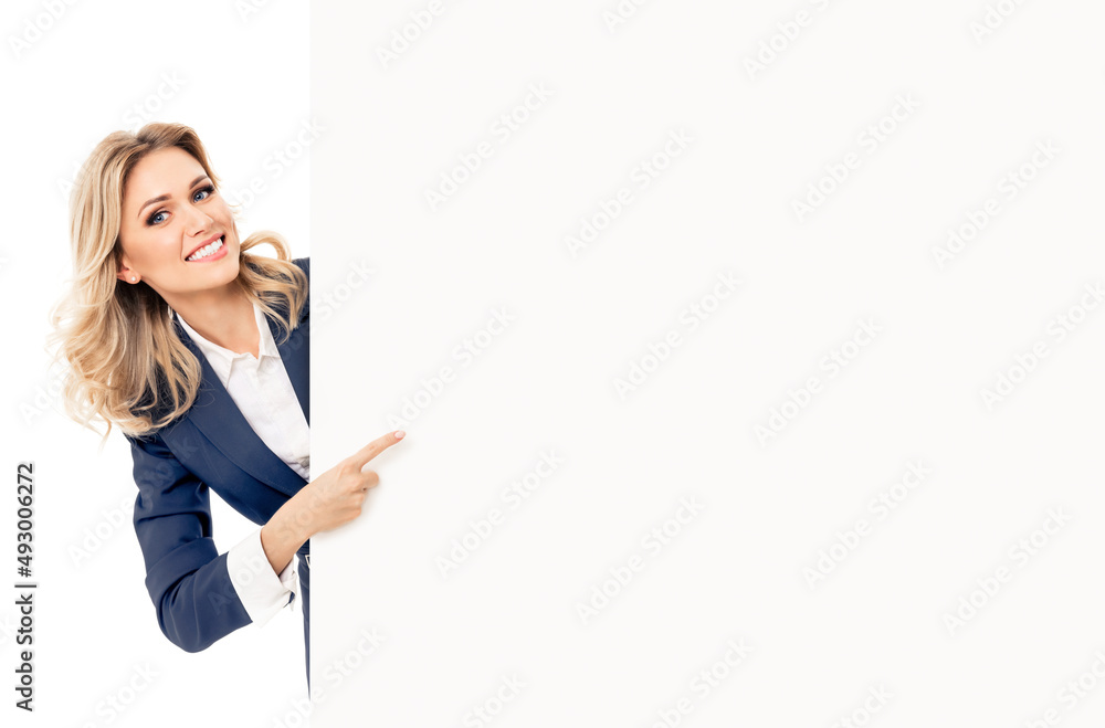 Happy smiling blond young business woman in blue suit, standing behind, peeping from blank banner or mock up signboard, showing copy space, isolated over white background. Happy smiling blond young business woman in blue suit, standing behind, peeping from blank banner or mock up signboard, showing copy space, isolated over white background.