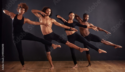 Perfectly poised. A group of dancers performing a dramatic pose in front of a dark background.