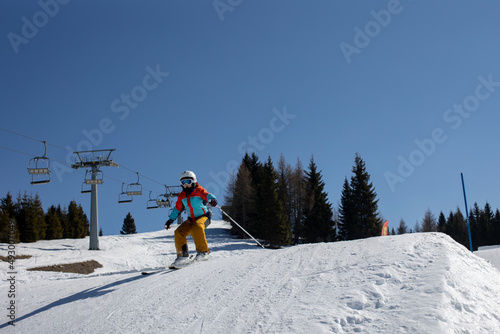 Happy preteen child, jumping with ski in a snow fun park. Kid skiing in Italy on a sunny day, kids and adults skiing together