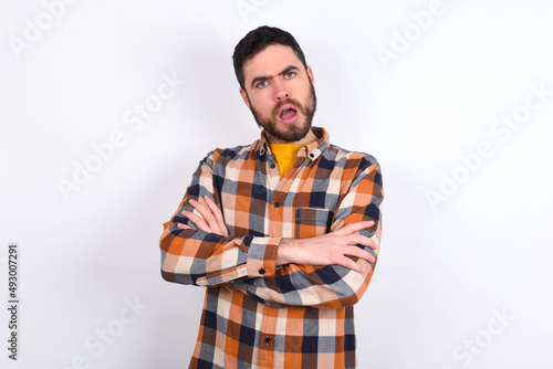 Shocked embarrassed young caucasian man wearing plaid shirt over white background keeps mouth widely opened. Hears unbelievable novelty stares in stupor photo