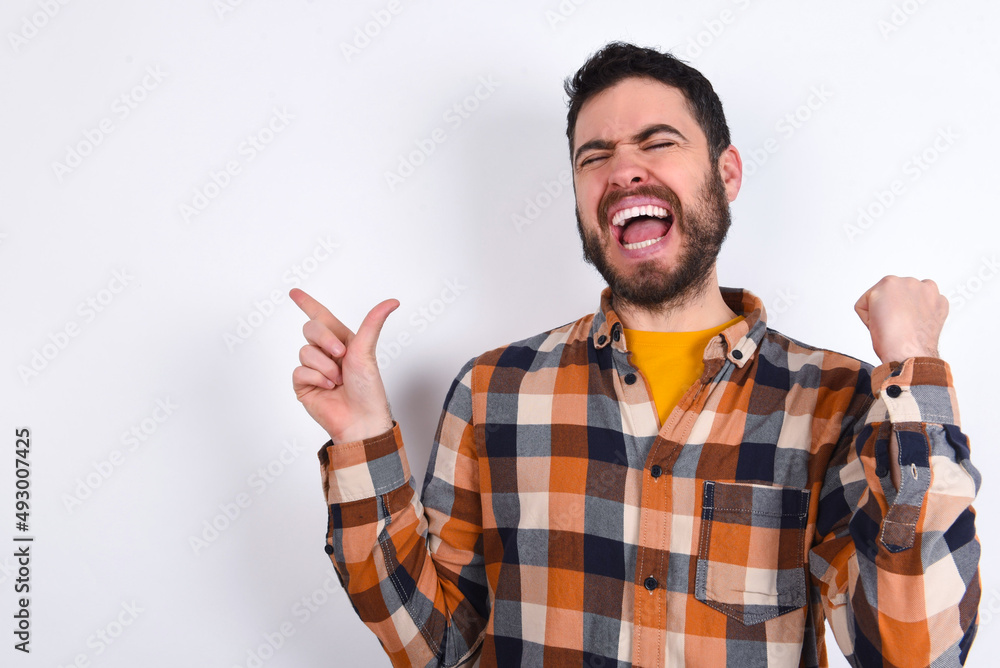Fototapeta premium Cheerful young caucasian man wearing plaid shirt over white background showing copy space ad celebrating luck