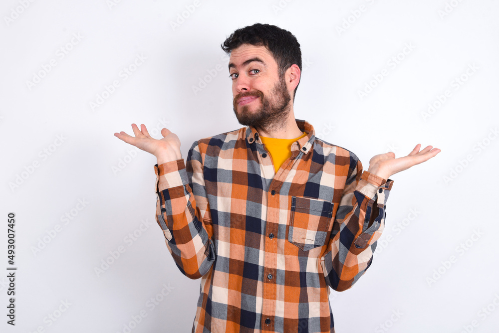 Careless attractive young caucasian man wearing plaid shirt over white background shrugging shoulders, oops. Careless attractive young caucasian man wearing plaid shirt over white background shrugging shoulders, oops.