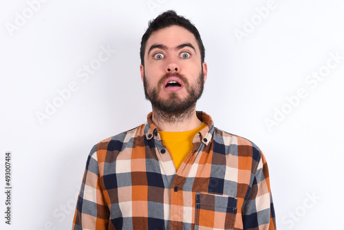 Shocked young caucasian man wearing plaid shirt over white background stares bugged eyes keeps mouth opened has surprised expression. Omg concept