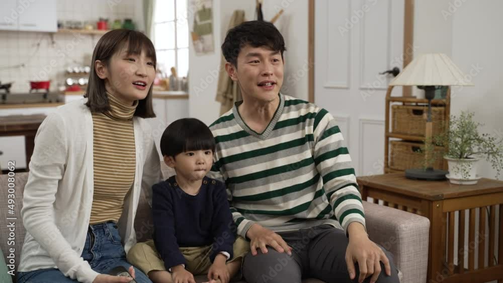happy Asian family of three having fun watching television together at home. cute boy laughing with his father and mother while they are pointing at the tv happy Asian family of three having fun watching television together at home. cute boy laughing with his father and mother while they are pointing at the tv