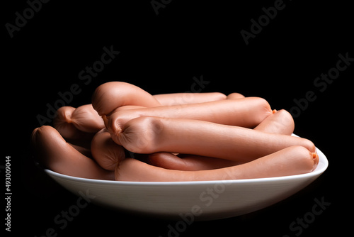 Hot dog sausages on a white plate on a black background with copy space