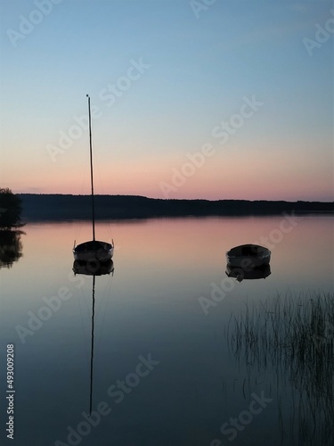 Two boats are reflected on the surface of a lake in a pink sunset.
