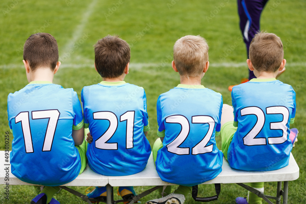 Fototapeta premium School football team. Soccer players sitting on sideline bench. Youth soccer players sitting together on substitute bench and watching match