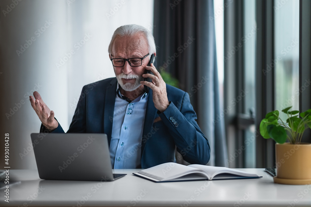Φωτογραφία Portrait of mature senior businessman entrepreneur in casual business office making phone call and gesturing while working with laptop and examining, looking, going through data and reports