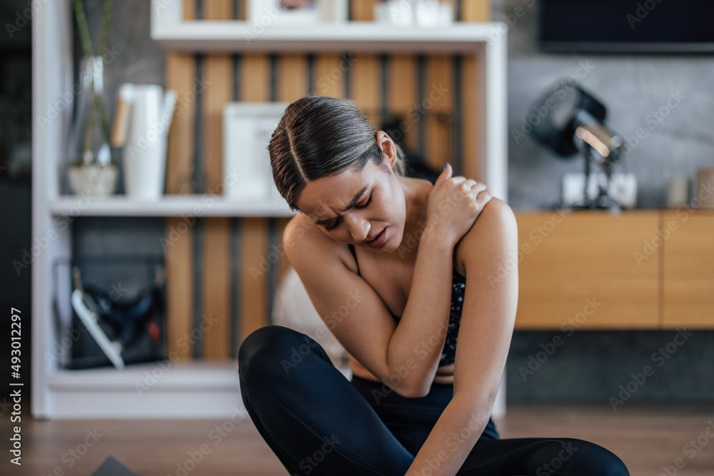 Girl having shoulder pain, sitting on a sports mat. Girl having shoulder pain, sitting on a sports mat.