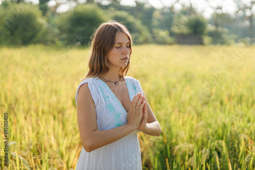 Pregnant woman stand at the field with green grass and fold her hands in pray. Sunshine summer vibes