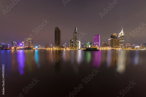 Ho Chi Minh City skyline and Saigon river port at night featuring key buildings, colorful lights and boat traffic. This is the financial center of Vietnam and Southeast Asia.