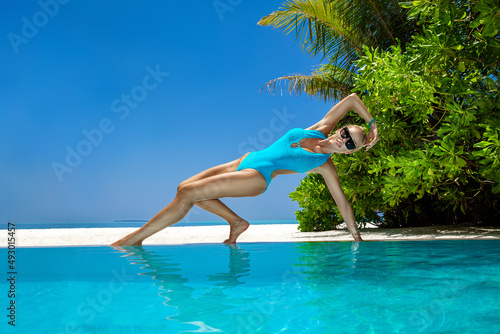 Sexy woman in bikini at Maldives tropical sand beach. Young glamour model in swimsuit near the pool. Perfect body bikini model long blonde hair. Bikini fashion. Luxury travel.