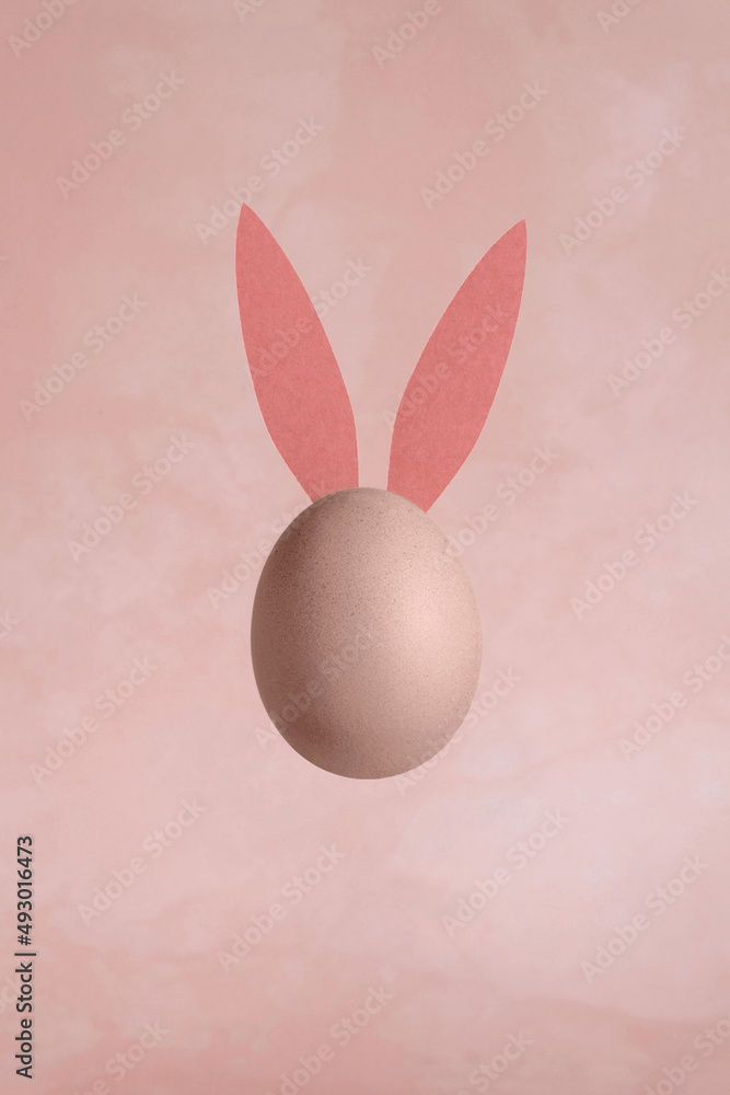 Single Egg with Bunny Ears on a Grunge Light Pink Background. Modern Minimalist Easter Holiday Composition with Chicken Egg ideal for Banner, Card, Greetings. Top View. No text. Funny Levitating Egg. Single Egg with Bunny Ears on a Grunge Light Pink Background. Modern Minimalist Easter Holiday Composition with Chicken Egg ideal for Banner, Card, Greetings. Top View. No text. Funny Levitating Egg.