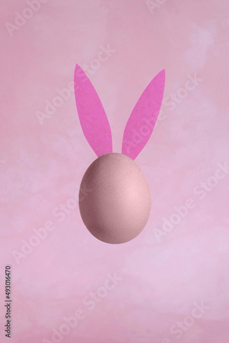 Single Egg with Bunny Ears on a Grunge Light Pink Background. Modern Minimalist Easter Holiday Composition with Chicken Egg ideal for Banner, Card, Greetings. No text. Funny  Levitating Egg. © Magdalena