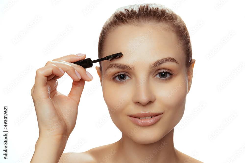 Portrait of young beautiful woman with natural makeup using brow mascara isolated over white studio background