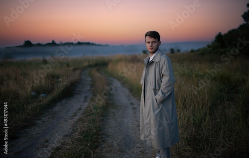 a man in a gray cloak alone in a field at sunset. © velimir