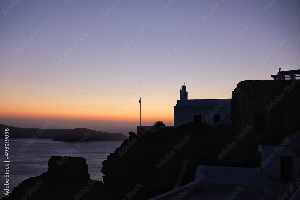 A small Greek Orthodox chapel at the top of the hill overlooking the Aegean Sea and a colorful sunset in Santorini