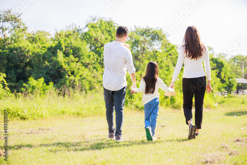 happy family life concept. Asian parents (Father, Mother) and the little girl walking and have fun and enjoyed ourselves together on a sunny day. family relaxes in the green park. Family weekend.